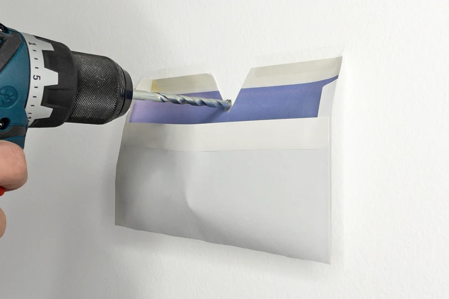 Um das Bohrmehl aufzufangen, wird ein Briefumschlag an die Wand geklebt.